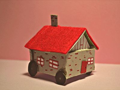 바퀴가 달린 빨간 지붕의 모형 집이 길 위를 달리고 있다.